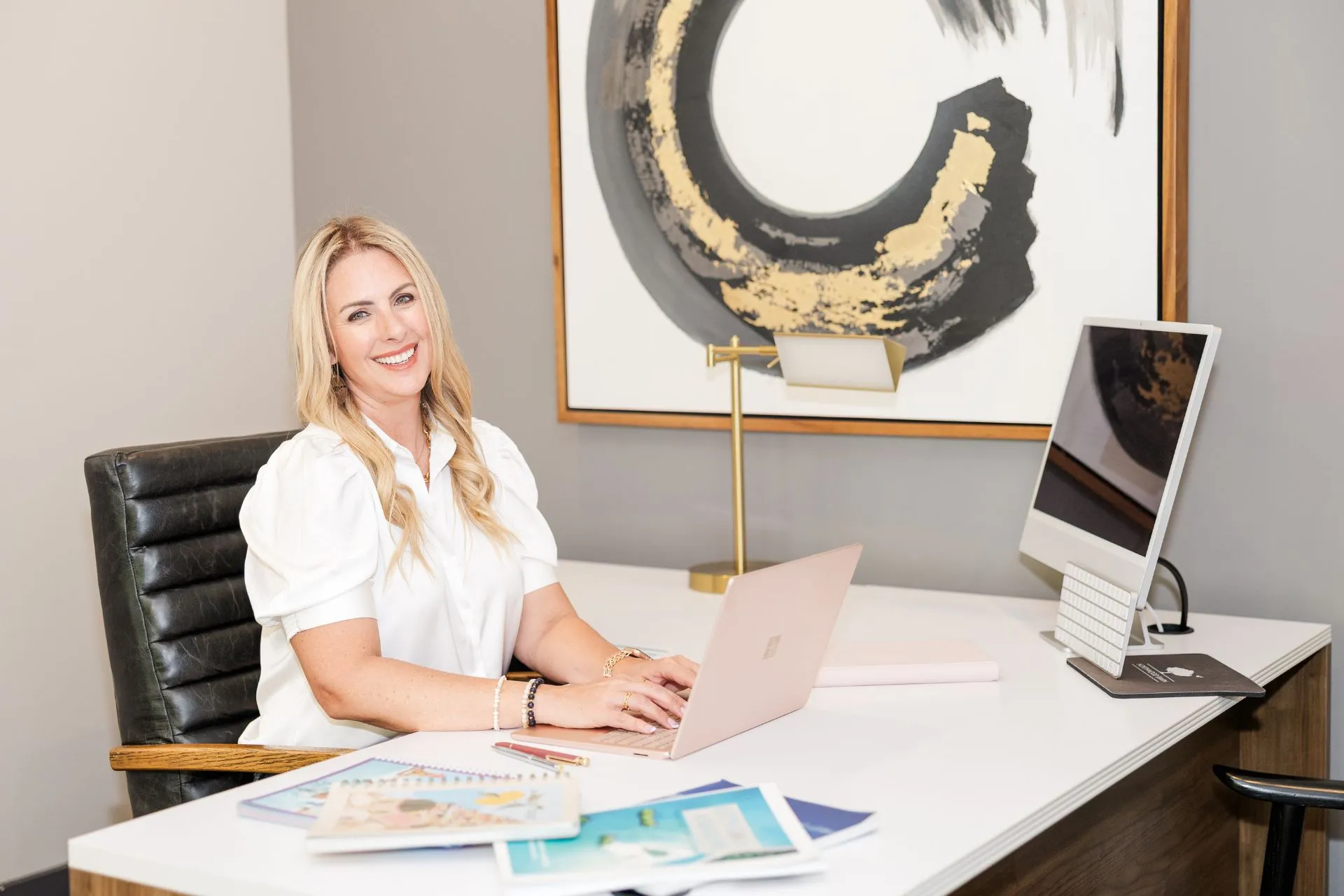 Woman working on a laptop at a modern desk in an office setting.